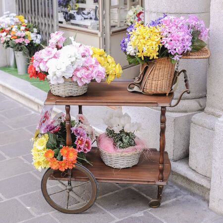 A cart with over wicker baskets and an old wicker fishing basket full of flowers for saleの写真素材