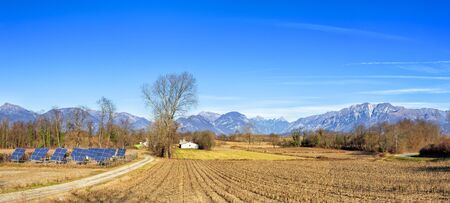 Agricultural winter panorama.  Small solar power station. Italian Alps in the background