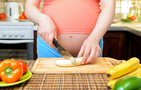 Pregnant woman prepares a banana in the kitchen. Healthy food.の写真素材