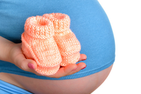 Pregnant woman holding a beautiful woolen baby shoes isolated on white
