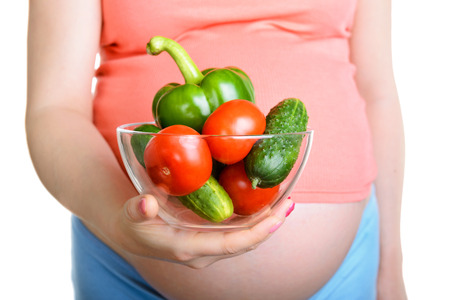 Pregnant woman holding a fresh vegetables isolated on white backgroundの写真素材