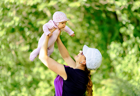 Happy mother throws up baby in nature on blurred backgroundの写真素材