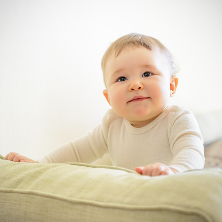 Baby girl plays on the couch at home. Baby attentively looks.