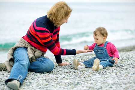 Baby girl and her mother playing with pebbles on the beachの写真素材