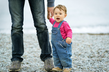 Baby girl and her father on the sea beach. Father holds daughter's hand.の写真素材