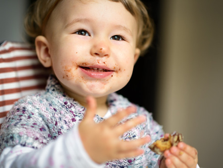 Eating cheerful baby girl with messy face. The funny one-year child eats and smiles.