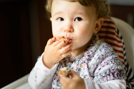 Eating baby girl with messy face. The one-year child eats and puts fingers in his mouth.の写真素材