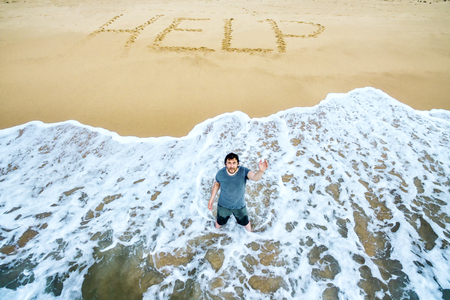 A man is calling for help on the beach of an uninhabited island. Inscription HELP on the sand.の写真素材