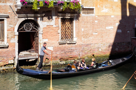 Venice, Italy - May 21, 2017: The gondola with tourists floats along the old canal in Venice. Gondola is the most attractive tourist transport in Venice. Romantic water trip across streets in Venice.のeditorial素材