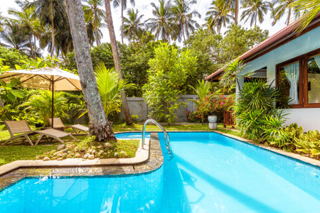 Sri Lanka - November 4, 2017: Pool with umbrella and beach beds in backyard of luxury tropical hotel. Beautiful swimming pool with blue clean water in courtyard. A relax in the sunny idyllic garden.のeditorial素材