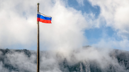 Russian flag overlooking Mount Ai-Petri in Crimea, Russia. Waving Russian flag on the cloudy blue sky background.の写真素材