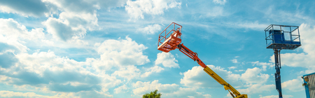 Cherry pickers on blue sky background. Boom with lift buckets of heavy machinery. Panoramic view of the platforms of the telescopic construction lifts in summer.の写真素材