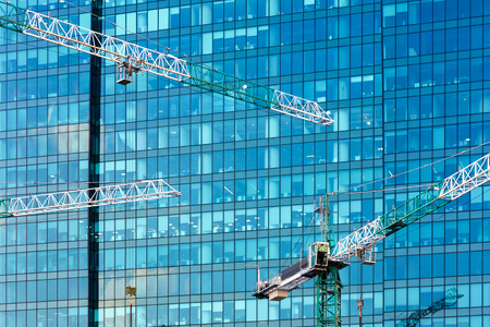 Construction cranes on the background of modern building. Glass facade of skyscraper at the construction site.の写真素材