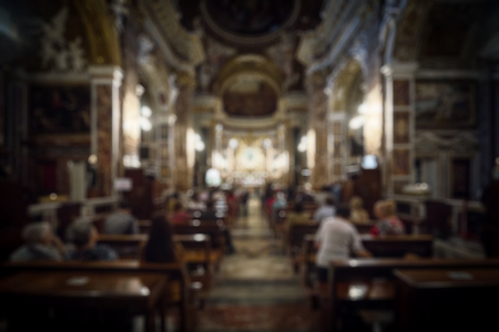 Interior of Catholic church as abstract creative blur background. People sit on the pews in front of...