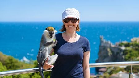 Young woman posing with a monkey on the Black Sea coast of Crimea, Russia. Female tourist relaxing...