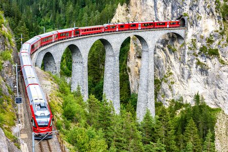 Landwasser Viaduct in Filisur, Switzerland. It is famous landmark of Swiss. Red express train on high bridge in mountains. Scenic view of amazing railway in summer. Concept of travel in Alpine Europe.の写真素材