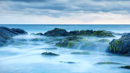 Long exposure of mystery ocean and rocks. Tropical landscape with surreal stones on sea beach. Scenic view of water like fog and mist. Beautiful panorama of magic nature in evening.の写真素材