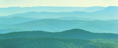 Mountain landscape background. Panoramic view of wild nature of Crimea, Russia. Scenery of green mountain ridges covered forest in light evening mist. Beautiful minimalist landscape in summer.の写真素材
