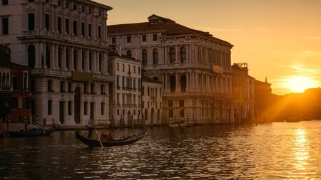 Venice at sunset, Italy. Gondola with tourists sails on Grand Canal at night. Panorama of Venice city in evening light. Scenery of sunny street in the Venice center. Romantic water trip at dusk.の写真素材