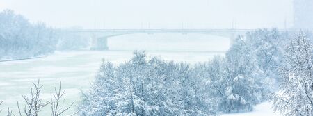 Winter landscape, Moscow, Russia. Scenery of snowy park by frozen Moskva River during snowfall. Winter nature background. Panoramic view of beach and bridge under snow. Frost and snowstorm in city.の写真素材
