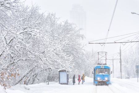 Winter landscape in winter, Moscow, Russia. Frozen tram on snowy street. People wait transport at ice stop. Cold and snowfall in city. Road under snow during snowstorm. Frost and blizzard concept.の写真素材