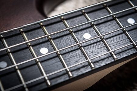 Bass guitar with four strings closeup. Detail of popular rock musical instrument. Close view of brown electric bass, selective focus. Macro photo of textured neck and frets of bass guitar.の写真素材