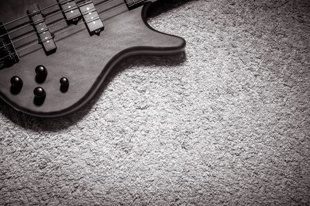 Bass guitar with four strings in black and white. Detail of popular rock musical instrument. Top view of wooden textured electric bass on carpet. Vintage style photo of bass guitar for background.の写真素材