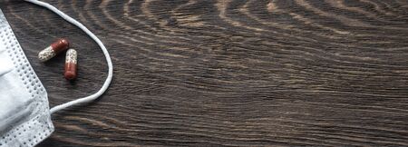 Panoramic view of medical mask and pill capsules for treatment on wooden table.の写真素材