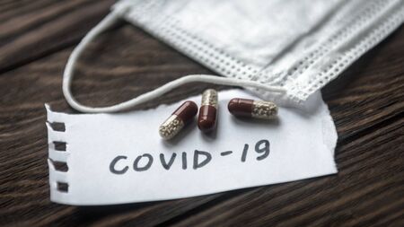 COVID-19 coronavirus concept. Protective mask and pill capsules for treatment of COVID-19. Novel corona virus outbreak, epidemic spread in world. Coronavirus medicine on wooden table.の写真素材