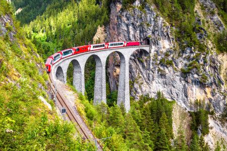 Landwasser Viaduct in summer, Filisur, Switzerland. It is landmark of Swiss Alps. Nice Alpine landscape. Red train of Bernina Express on railroad bridge in mountains. Scenic view of famous railway.のeditorial素材