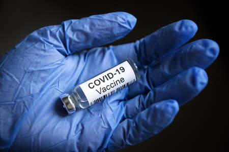 COVID-19 vaccine in gloved hand, doctor holds bottle with vaccine for coronavirus cure in palm. Concept of corona virus research, protection, treatment and clinical trial during coronavirus pandemic.の写真素材