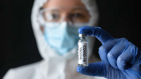 COVID-19 vaccine in doctor's hand, nurse in medical personal protective equipment (PPE) holds bottle with vaccine for coronavirus cure. Concept of corona virus treatment during coronavirus pandemic.の写真素材