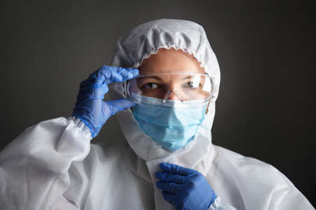 Doctor in personal protective equipment (PPE), woman wearing medical glasses and face mask, portrait of nurse in professional suit due to COVID-19 coronavirus pandemic. Care and safety concept.の写真素材