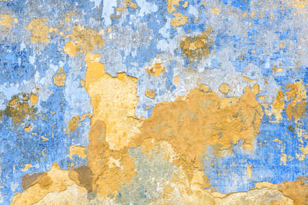 Old wall texture background, broken plaster for backdrop or wallpaper. Rough peeling stone wall surface painted in yellow and blue colors. Cracked grungy stucco abstract background.の写真素材