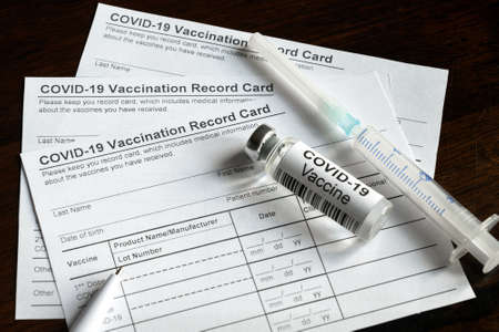 COVID-19 Vaccination Record Card on desk, coronavirus immunization certificate and vaccine injection. Syringe and vaccine bottle for corona virus are on medical form required for travel and tourism.の写真素材
