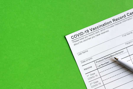COVID-19 Vaccination Record Card on green background, coronavirus immunization certificate with copy space. Top view of paper medical form required for travel. Concept of corona virus vaccine ..の写真素材