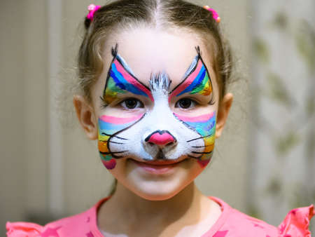 Kid with face painting of kitty, cute little girl with painted mask on her face of rainbow cat....