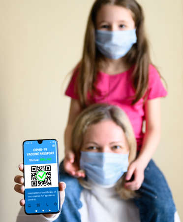 COVID-19 vaccination passport in mobile phone, happy woman with kid holds smartphone with health certificate app, digital coronavirus pass. Concept of corona virus, family and immunity passport.の写真素材