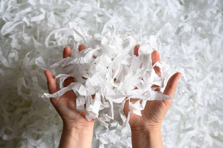 Shredded paper heap in hands, top view of many white strips. Pile of cut paper like confetti for party or box filler. Concept of recycle, waste, reuse and ecology.の写真素材