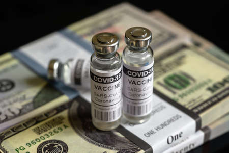 Vaccine vials from COVID-19 and dollar bill stacks, bottles with coronavirus drug on US money pile. Concept of vaccine price, expensive cost, fraud, business and rich during corona virus pandemic.の写真素材