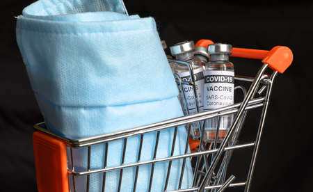 COVID-19 vaccine vials and medical masks in shopping cart, coronavirus medication in grocery trolley. Concept of safety, vaccine distribution, pharmacy, health and drugs during corona virus pandemic.の写真素材
