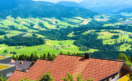 Scenery of rustic houses in Alpine green valley, Austria, Europe. Roofs in traditional village on background of mountain forest. Landscape of rural terrain in summer. Nature and vacation concept.の写真素材