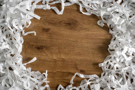 Frame of shredded paper on wooden table for background, top view of white paper strips heap. Flat lay with confetti and copy space for text. Concept of recycle, waste, ecology, data and party.の写真素材