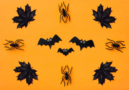 Halloween decorations on orange background, flat lay. Top view of bats, black spiders and maple...