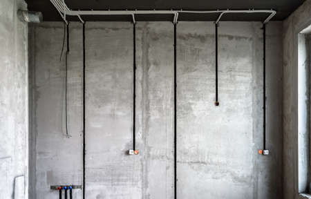 Electrical cables and pipes on house concrete wall. Modern plastic hoses and conduits with wires in...