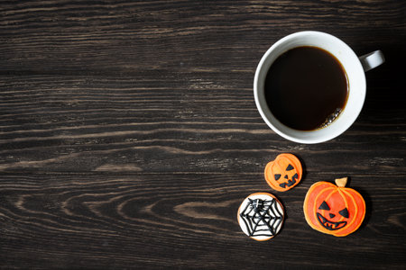 Halloween background, cup of coffee and sweets on wooden table, top view. Orange pumpkin shaped cookies on dark wood planks with space. Party, season, October, food, coffee and breakfast concept.の写真素材