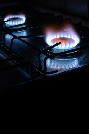 Gas stove at home, natural propane gas burns on dark background with black copy space, vertical view...