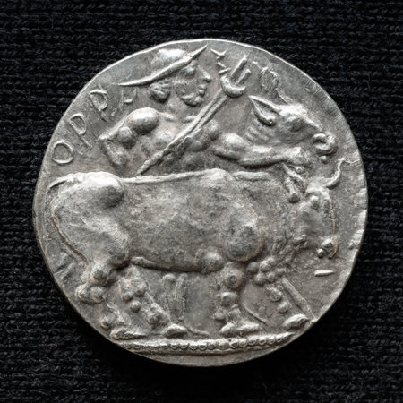 Ancient coin with image of bull, old rare money, silver artifact isolated on dark background, macro. Concept of Roman and Greek coin, past civilization, archeology, agriculture and history.の写真素材