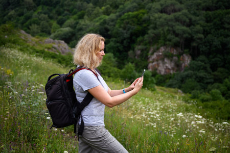 Woman hiker uses gps navigator app in smartphone walking in forest, person tourist look at mobile...
