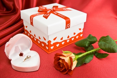 Gift and rose on the red background. Gold ring in the opened box.の写真素材